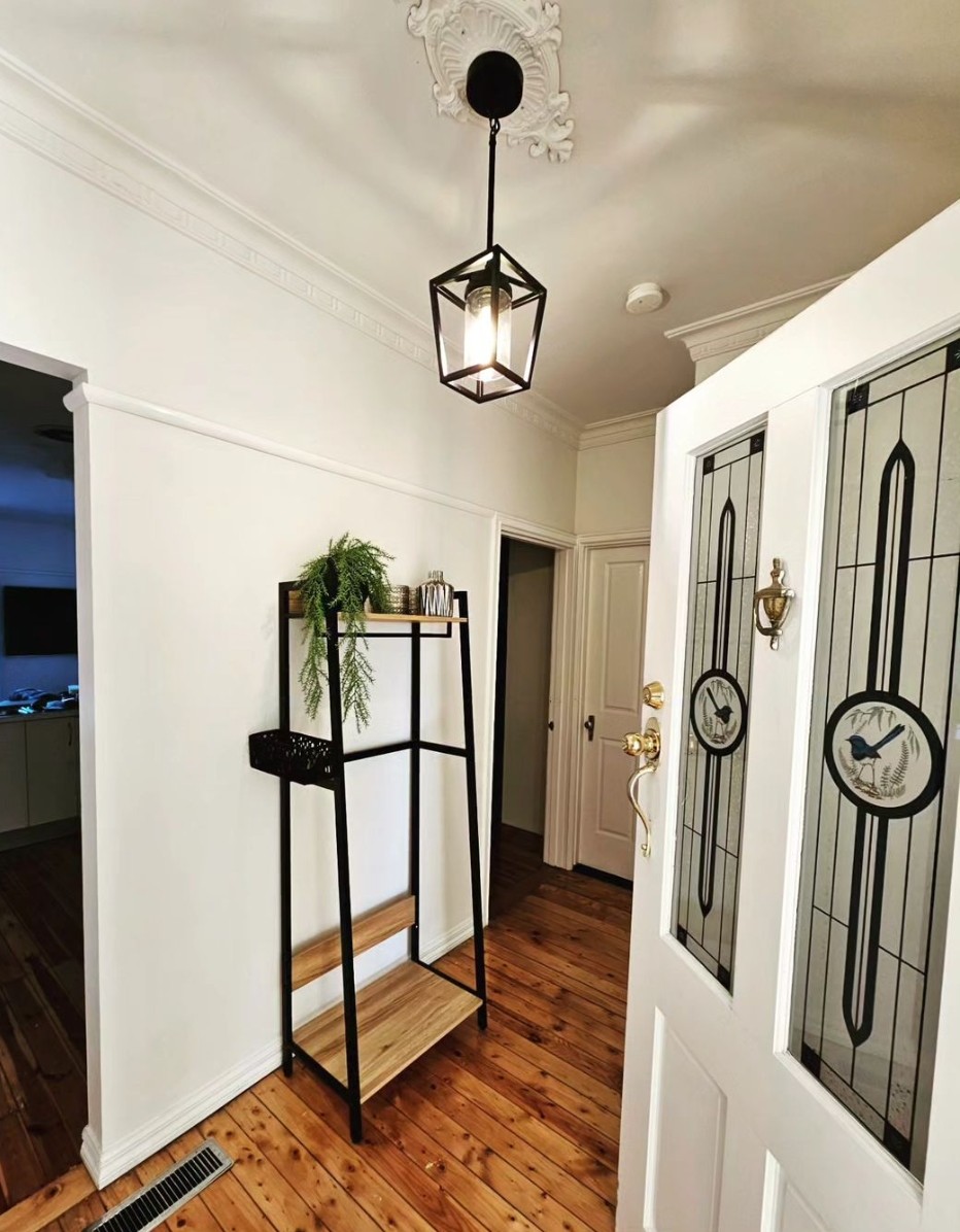 Black lantern pendant hung from an ornate ceiling rose in a period hallway with leadlight doors