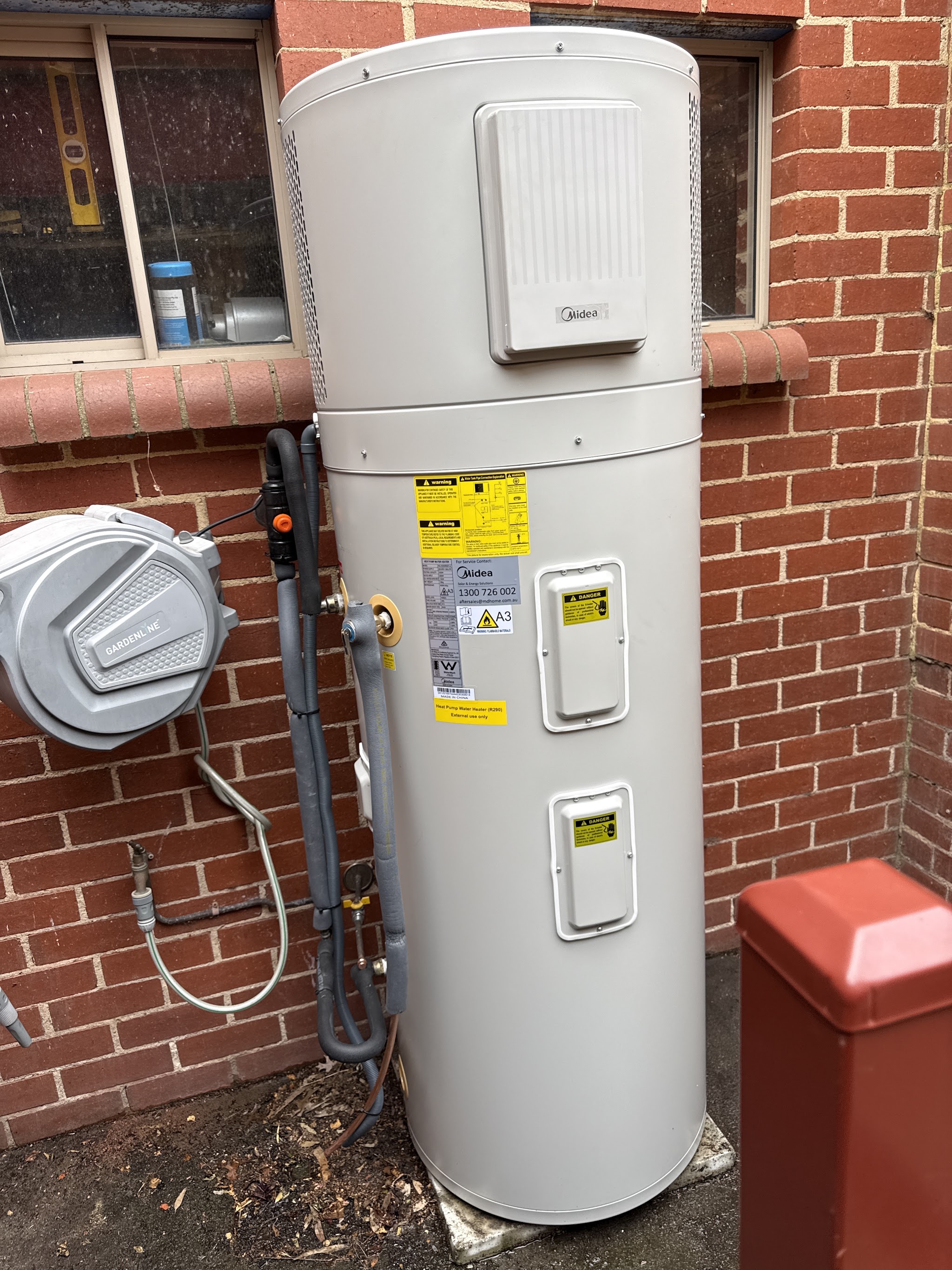 A completed heat pump hot water unit installed against a brick wall with lagged pipework