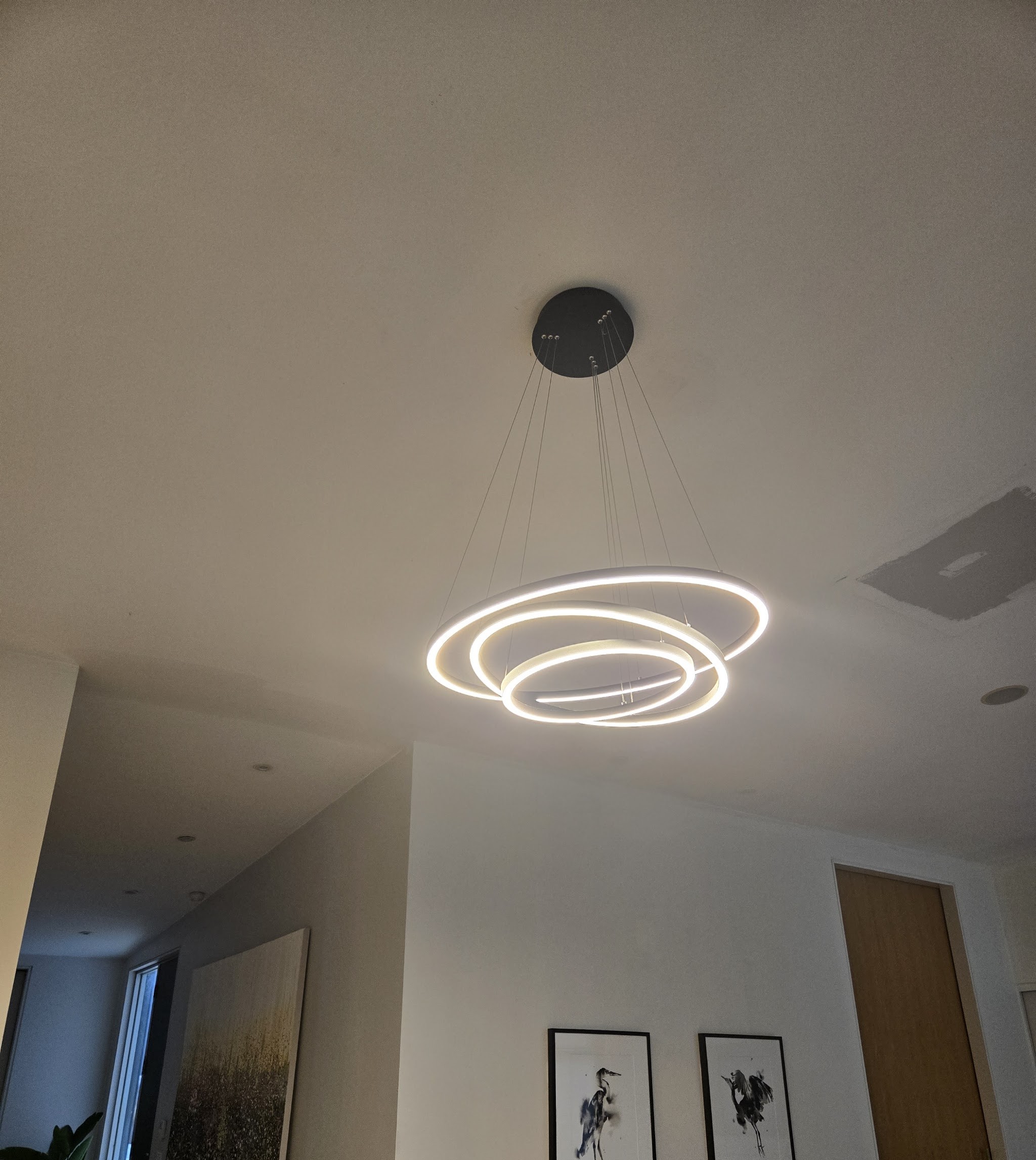 A large three ring LED pendant, lit, hanging in a modern hallway